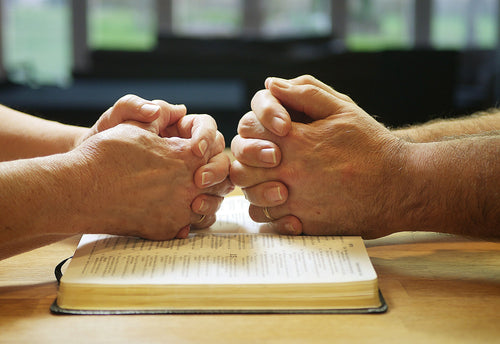 Husband and wife holding hands in prayer over an open Bible — His + Hers EVERYTHING Bundle by Paris Legacy Group
